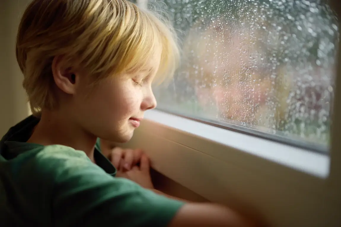 regulação emocional: menino de olhos fechados na frente de uma janela 