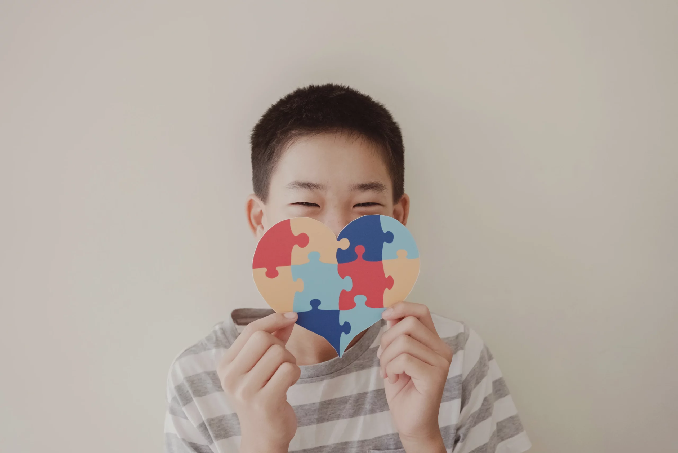 Dia Mundial da Conscientização do Autismo: menino com um coração constituído de um quebra-cabeça colorido.