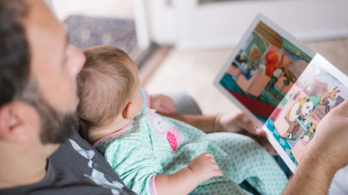Treinamento parental: pai segura bebê no colo e lê um livro
