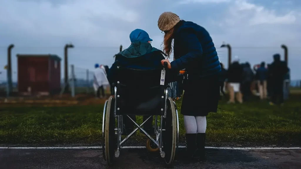 capacitismo: imagem mostra uma pessoa em pé e outra em uma cadeira de rodas. os dois estão de costas para a câmera e observam a paisagem