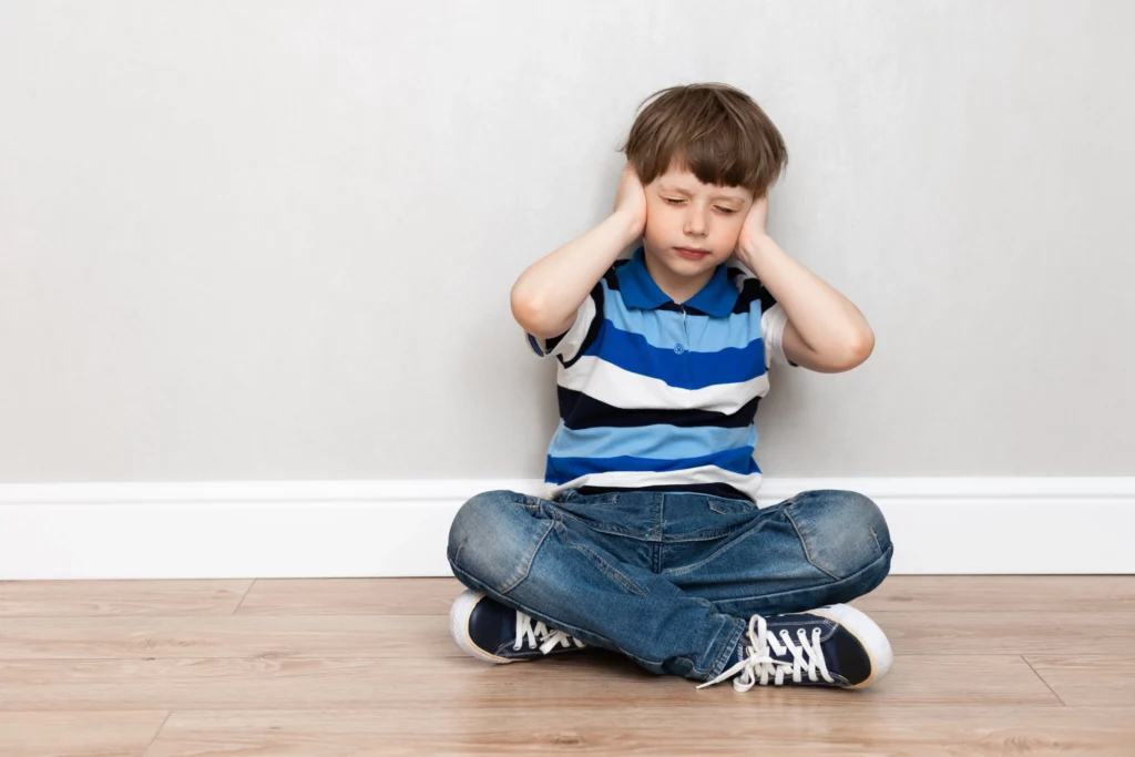 menino sentado no chão cobrindo os ouvidos 