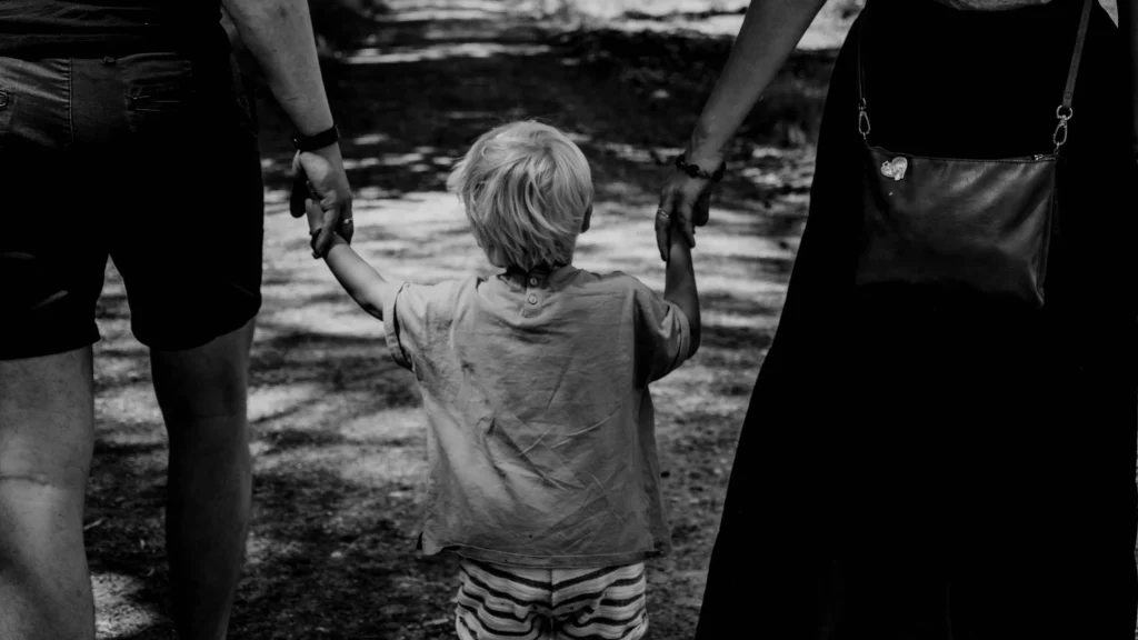 estresse parental: criança é segurada nas mãos pelos pais enquanto caminham