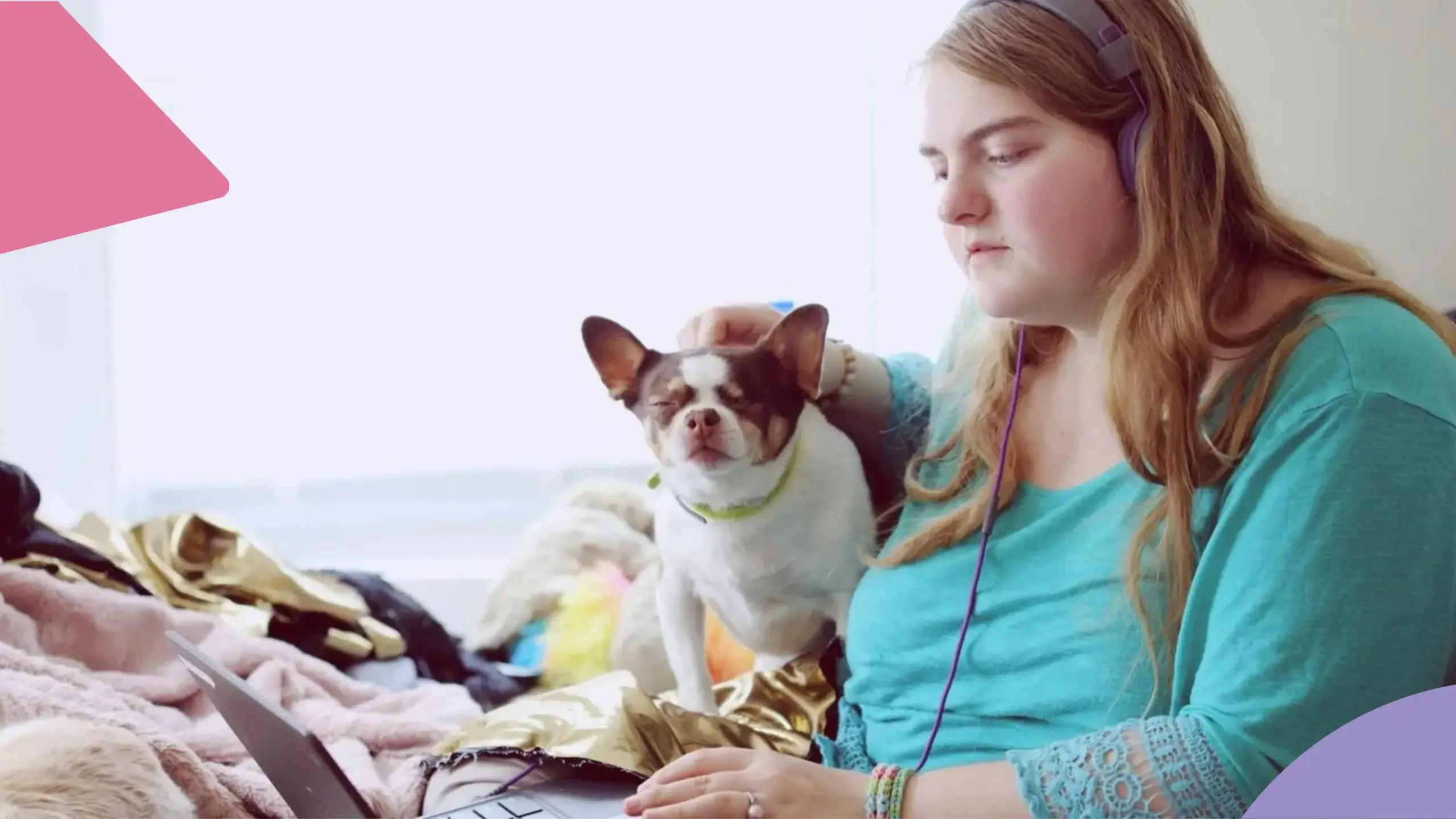 Mulher escutando música em um laptop. Ao seu lado, um cachorrinho recebe carinho dela