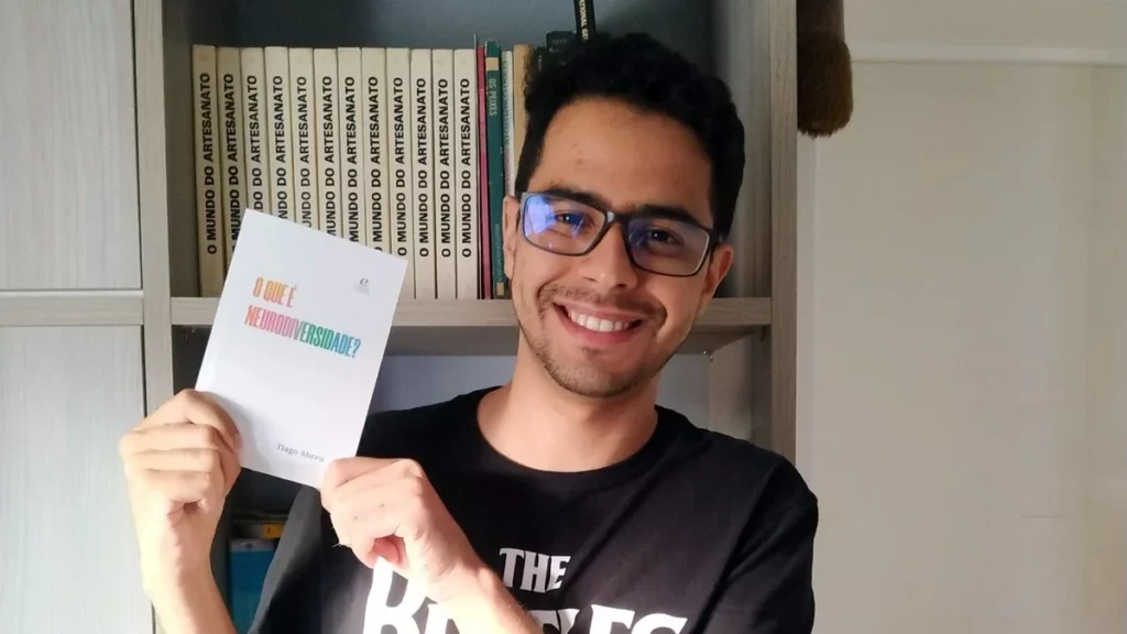 neurodiversidade: tiago sorri e segura o livro em suas mãos