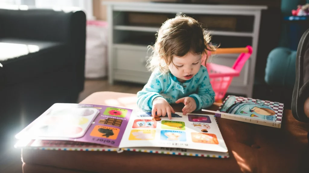 comunicação alternativa e aumentativa: menina está observando livro com figuras em quadrados e aponta para uma