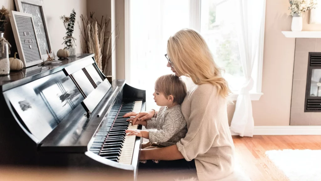 musicoterapia: imagem mostra mulher e criança sentados ao piano, la ajuda criança a tocar.