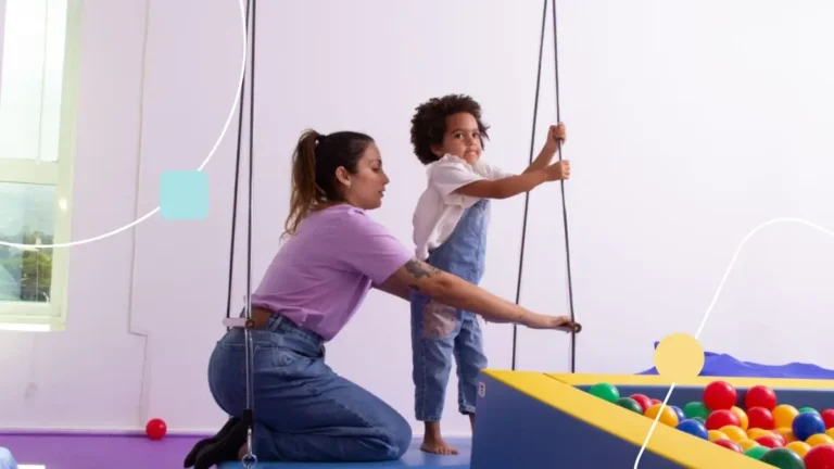Sessão de terapia ocupacional onde uma terapeuta está ensinando menina autista a brincar em cama elástica.