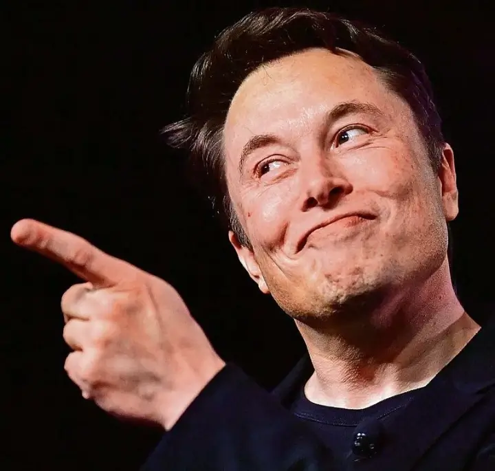 Elon Musk, apontando para frente com um sorriso no rosto
