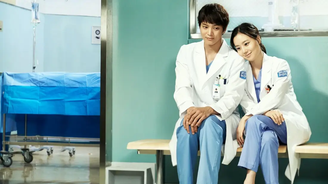 Dois médicos, um homem e uma mulher, sentados em um corredor de hospital.