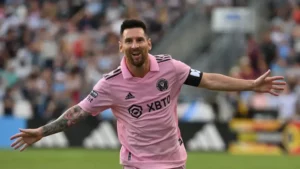Lionel Messi, jogador de futebol, celebrando um gol com os braços esticados e um sorriso no rosto.