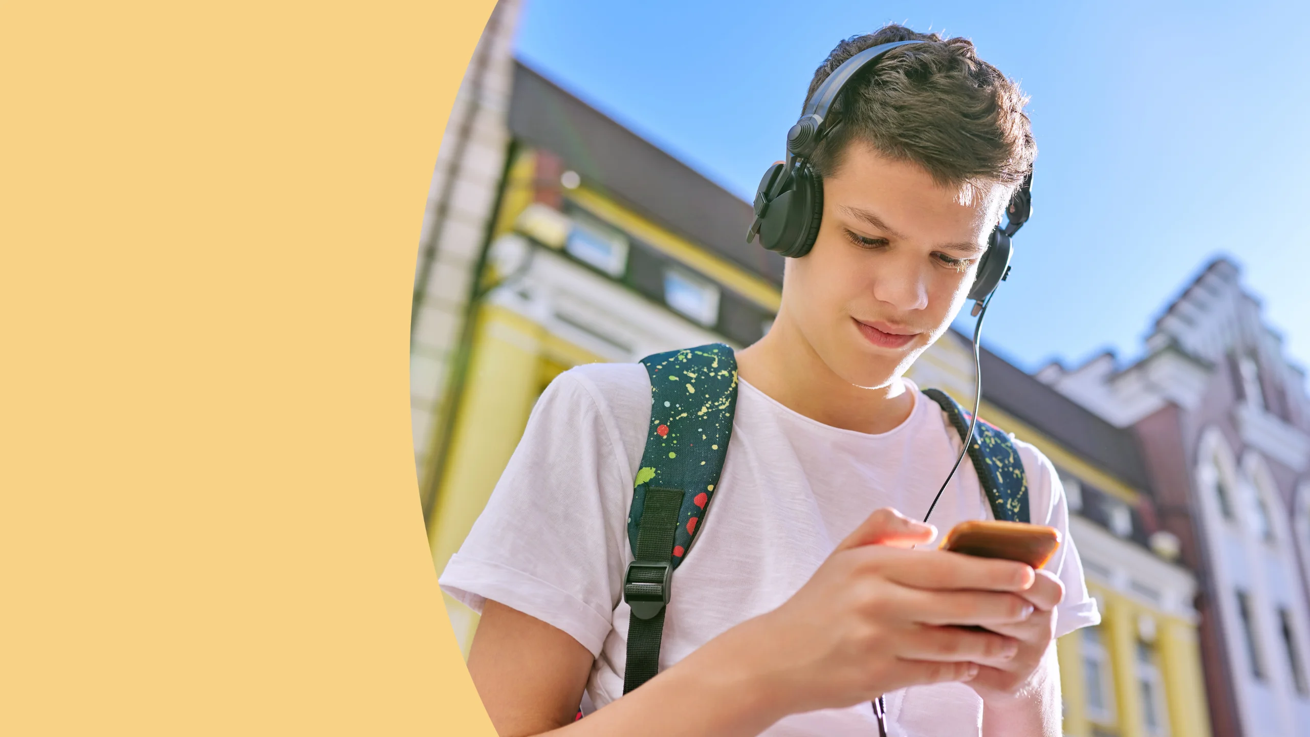 um menino adolescente aparece usando fones de ouvidos e olhando para um celular que está em sua mão