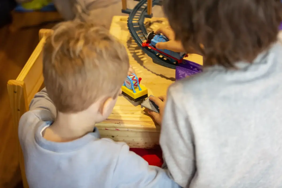 Crianças brincando com trens de brinquedo expostos sobre uma mesa.