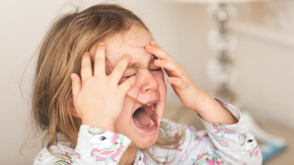 uma criança loira aparece gritando e chorando com a mão no rosto