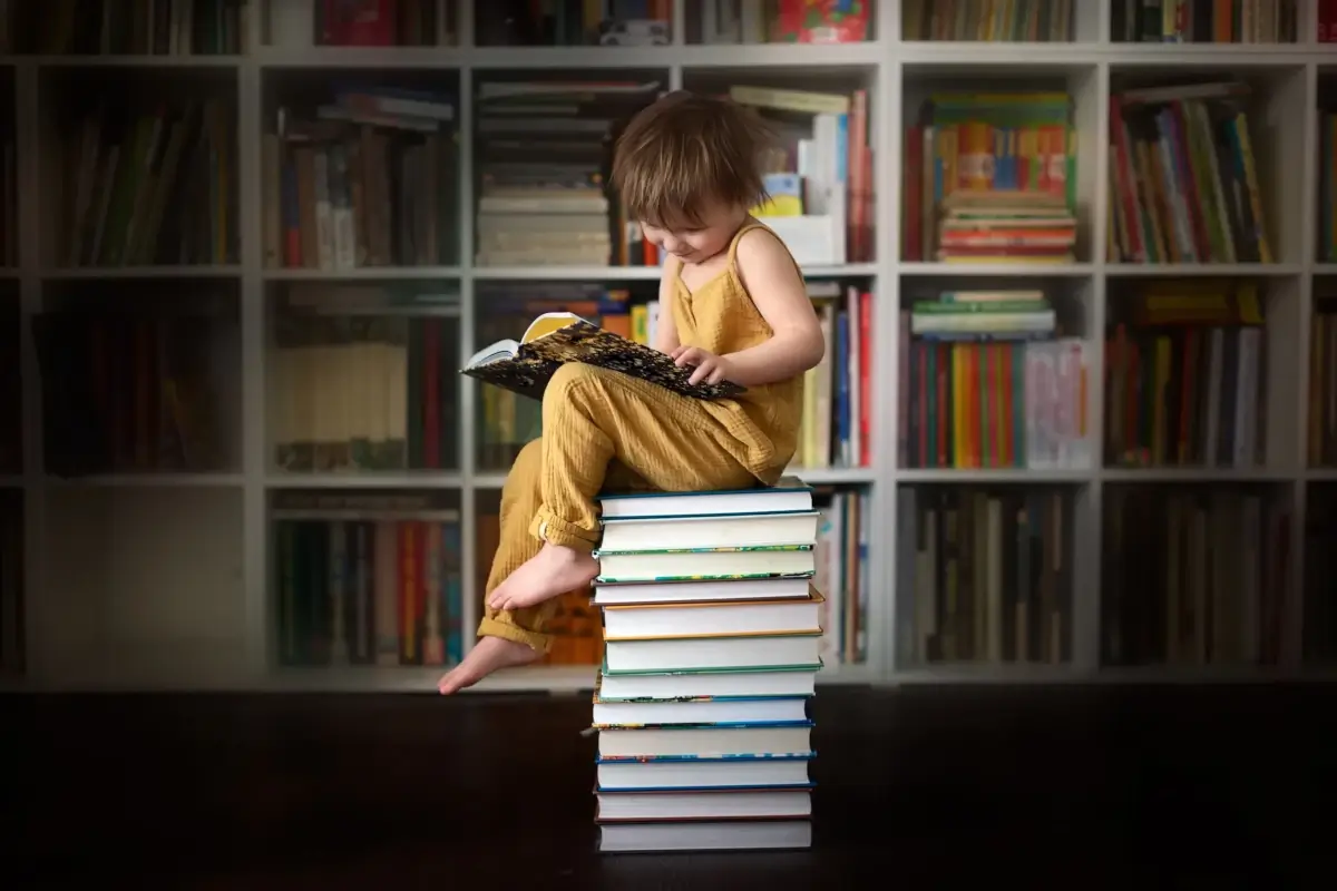 Criança sentada em uma torre de livros, em uma biblioteca.