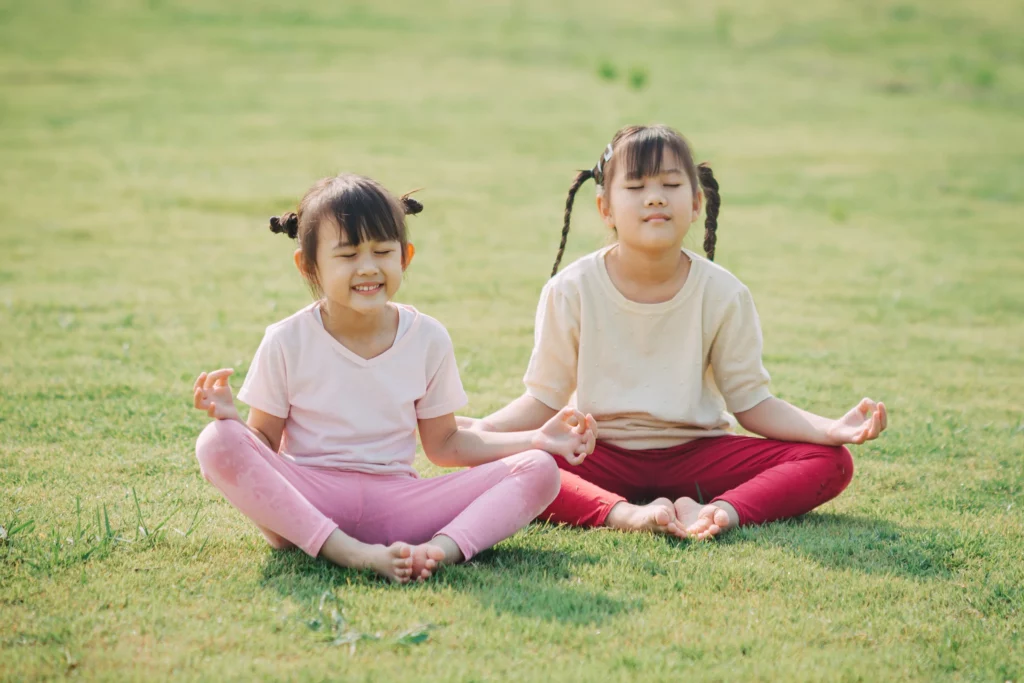 Atividades calmantes: 2 crianças sentadas na grama meditando