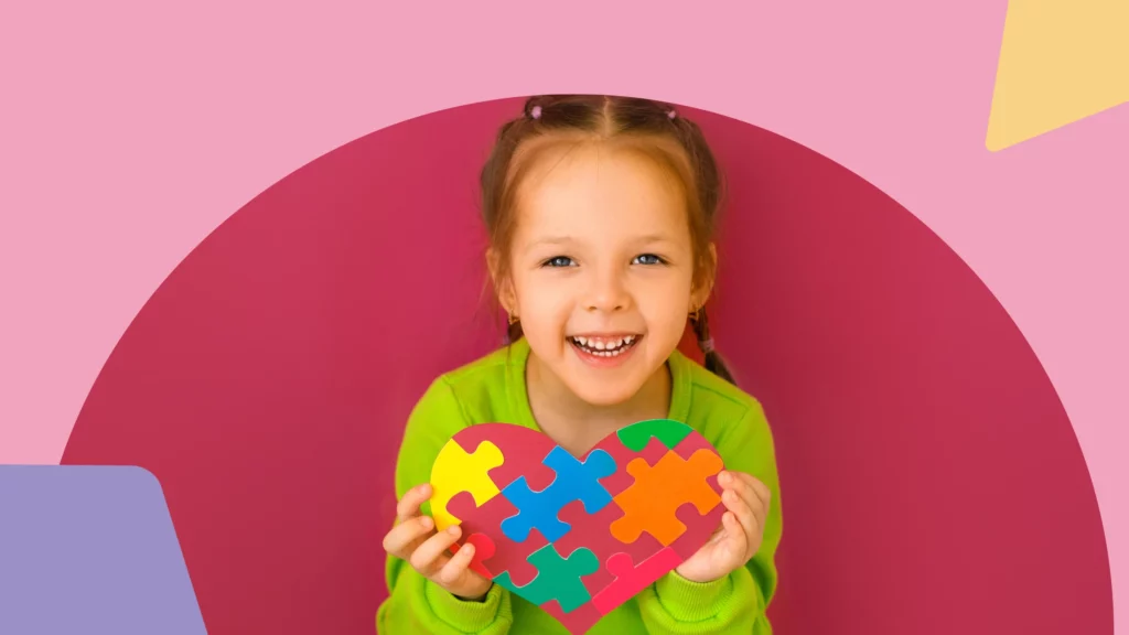 menina no espectro autista sorrindo segurando um coração colorido