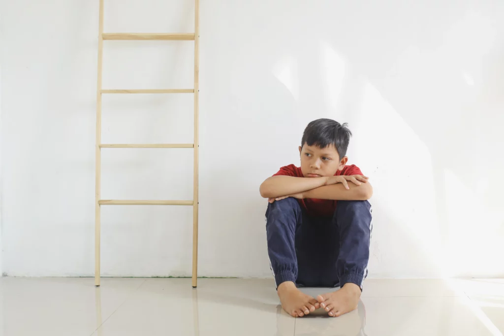 menino sentando no chão abrançando as pernas ao lado de uma escada