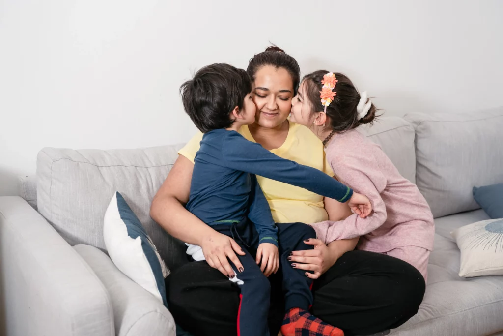 mãe sentada no sofá com seus filhos beijando sua bochecha 