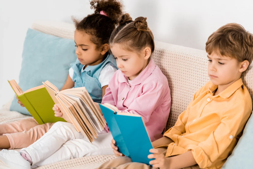 3 crianças sentadas no sofá lendo livros coloridos