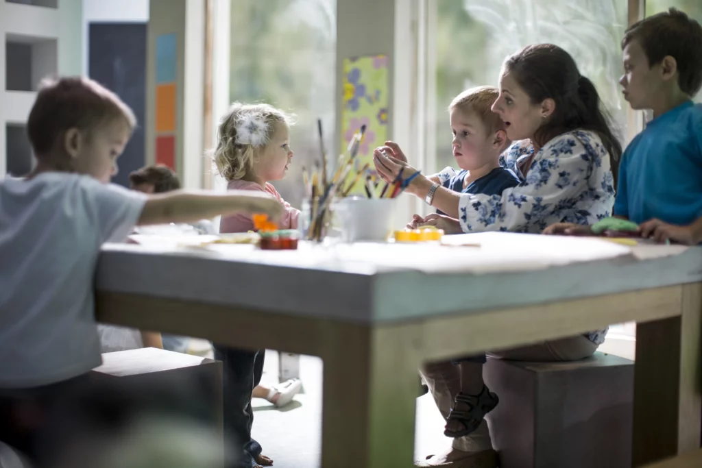 crianças na escola sentadas na mesa pintando com professora