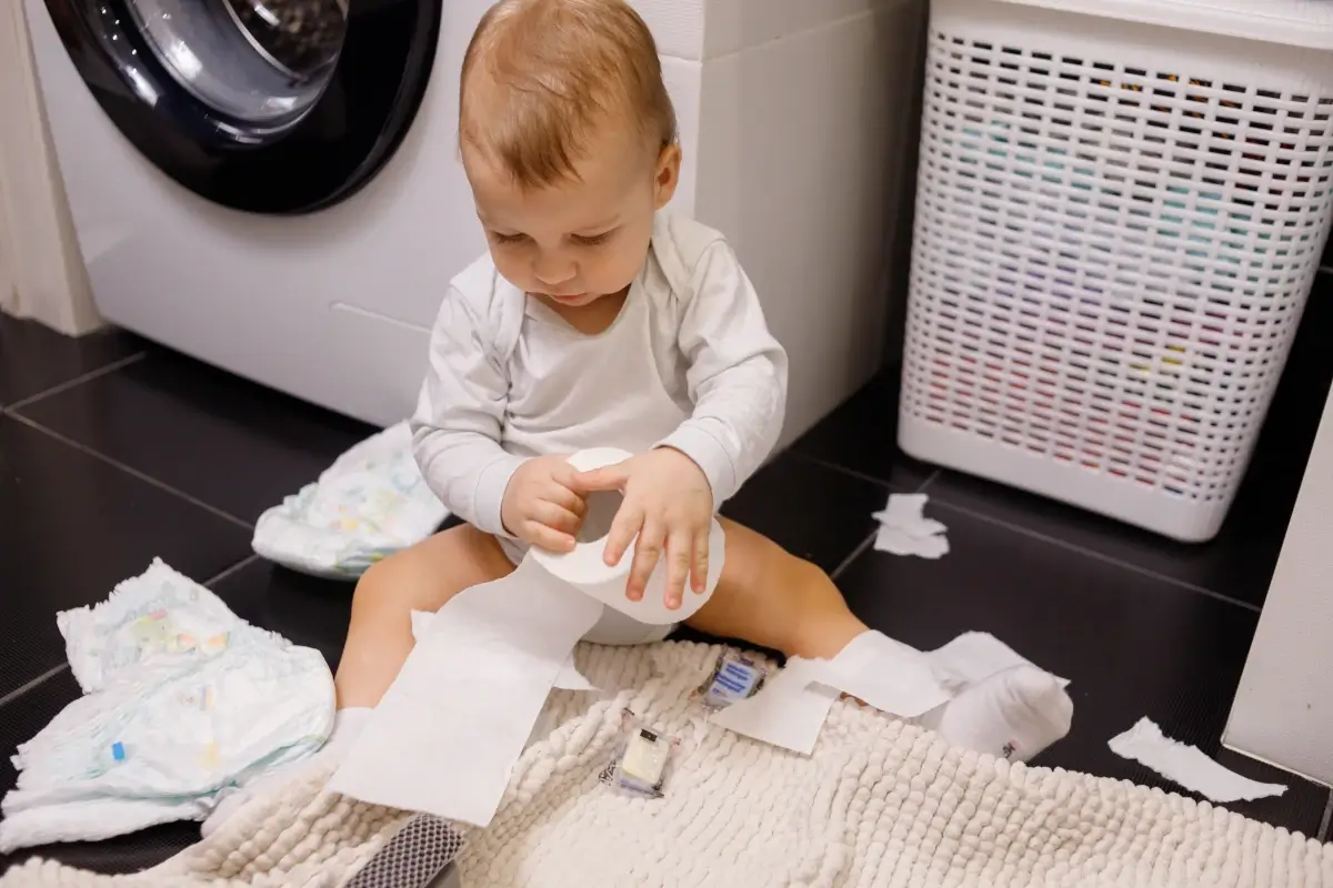 Bebê sentando ao chão, rasgando papel higiênico.