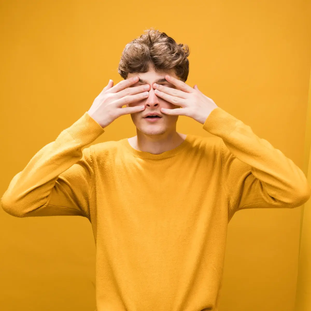 Contato visual no autismo: adolescente tapando os olhos. Tanto sua roupa, quando o fundo da imagem, tem tons de amarelo.