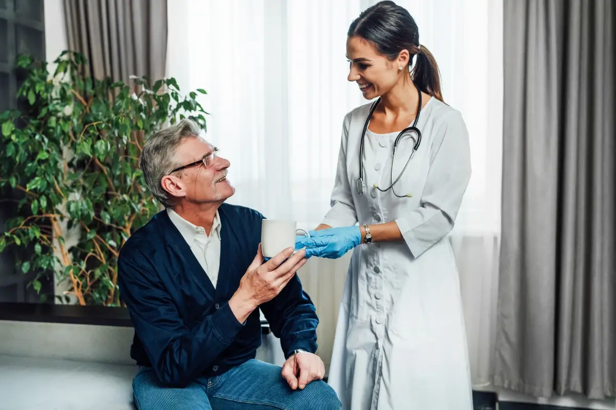 Anamnese: doutora conversando com paciente idoso. Ela e ele seguram uma xícara branca.