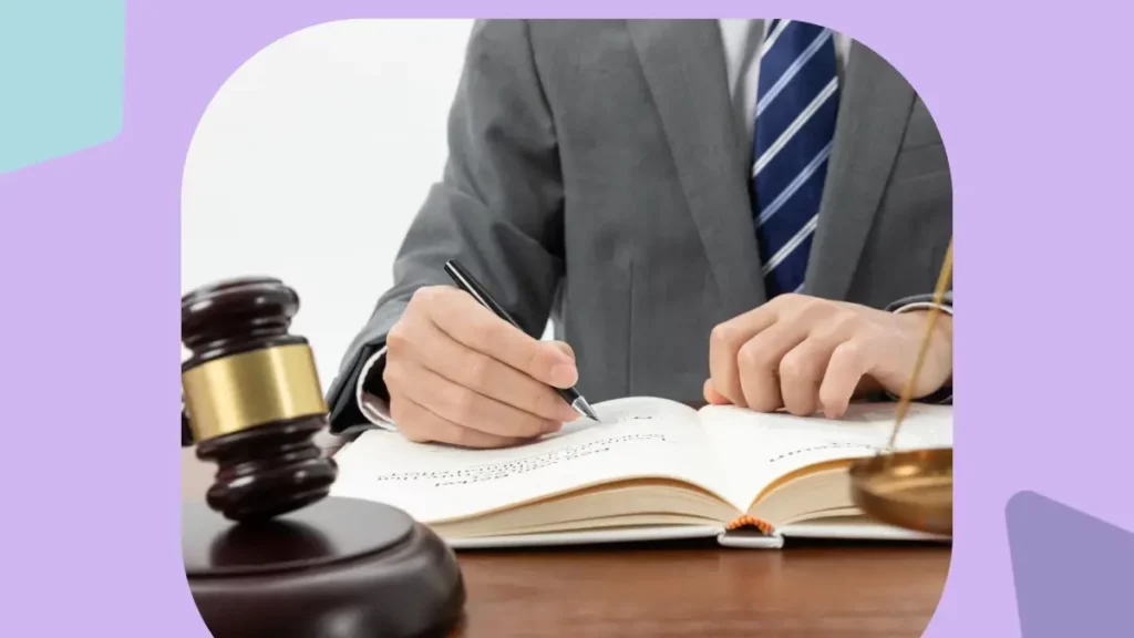 Homem de terno escrevendo em caderno com um martelo de Juiz a sua frente.