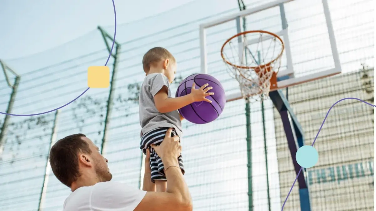 prática esportiva conhecida como Basquete. Pai levantando filho para que ele acerte a bola no cesto.