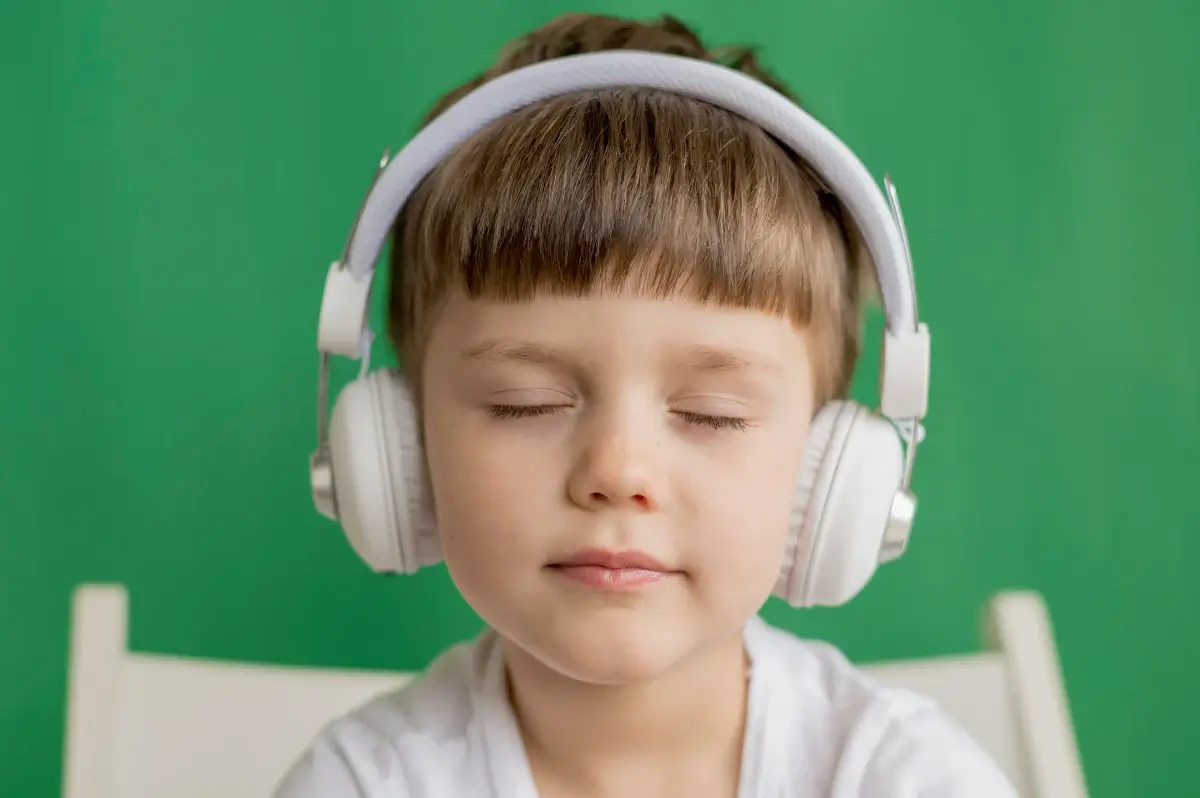 Retrato de uma rotina para criança autista: menino de olhos fechado com fone de ouvido. Ele tem um semblante relaxado e tranquilo.