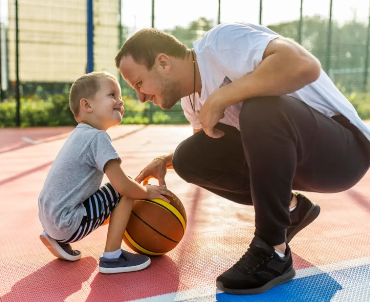Pai ensinando seu filho a jogar Basquete, prática esportiva.