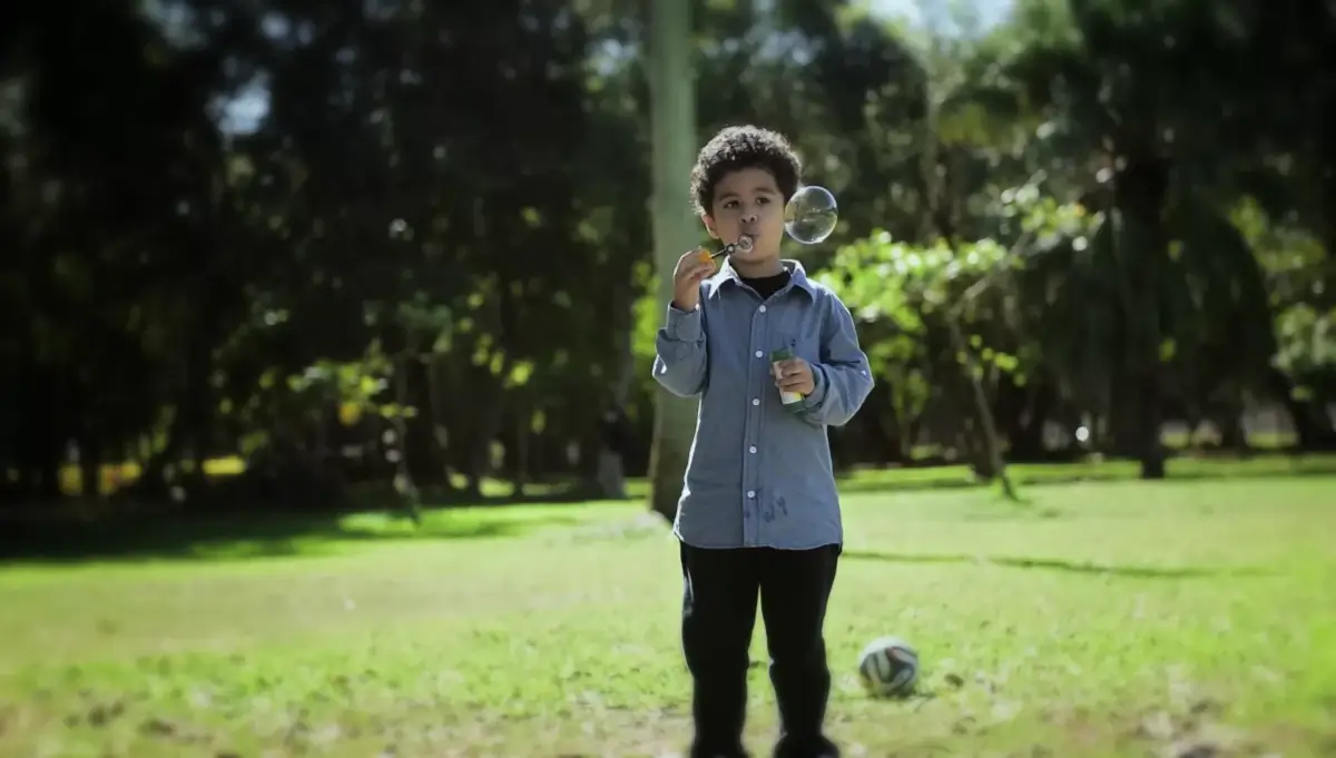 Menino brincando com bolhas de sabão em um parque arborizado. 