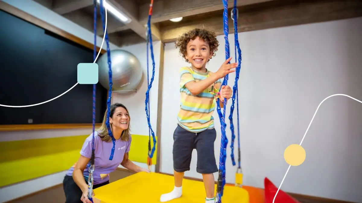 Imagem ilustrando a importância da terapia ocupacional no Autismo. Menino feliz brincando em balanço e terapeuta ao lado observando seu desenvolvimento.