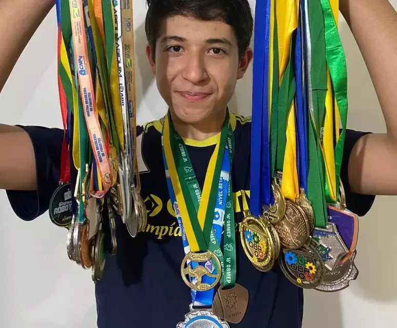 Alexandre Andrade de Almeida segurando diversas medalhas que ganhou em competições de ensino.