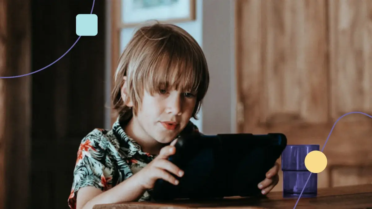 Criança com autismo leve sentada à mesa segurando um tablet.