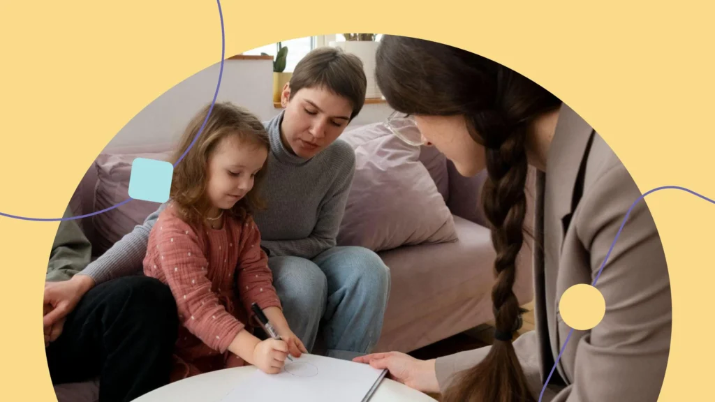 criança escrevendo em um papel ao lado da mãe e uma terapeuta