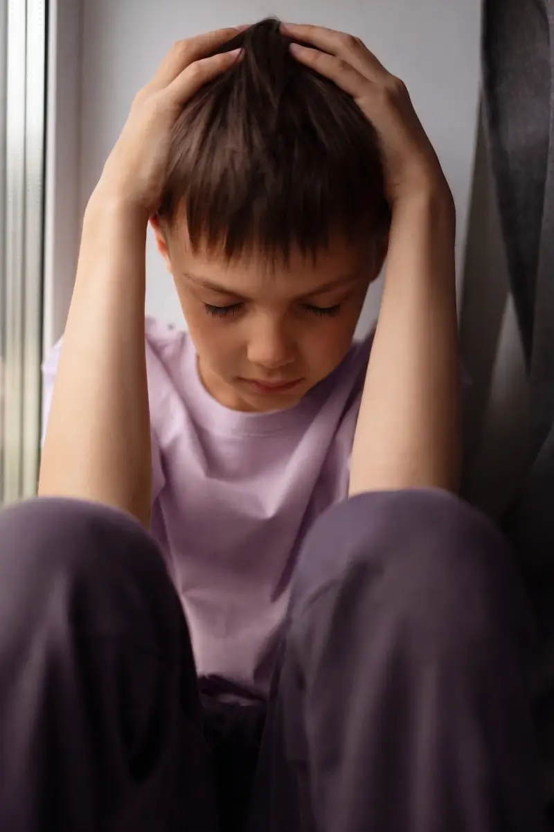 menino triste após uma crise. Ele está com as mãos na cabeça